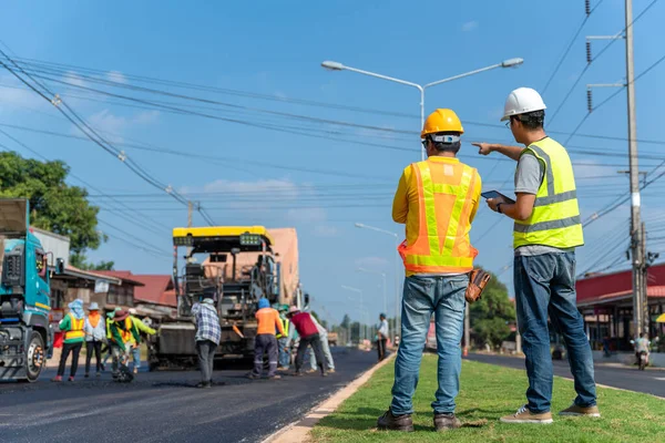 アジアの土木技術者は重機でフォアマンの進捗状況をチェックアスファルト舗装 道路ローラー 高速道路の建設修理を行うダンプトラック労働者 — ストック写真
