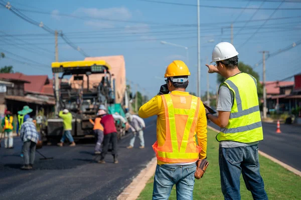 Civil engineer is assigning work to foreman\'s face with heavy equipment Asphalt paver & road roller & dump truck workers doing highway road construction repairs.