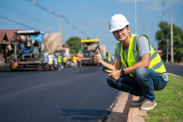 アスファルト舗装 道路ローラー ダンプトラックと労働者建設道路の背景と道路建設現場で提起親指で自信を示すアジアの若い土木技術者 — ストック写真