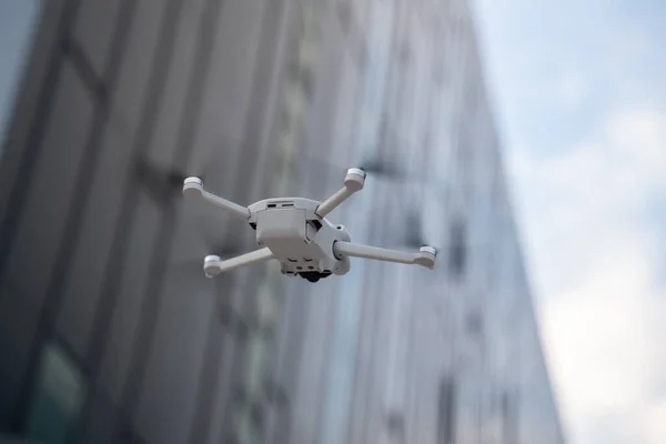 Small drone flies in a city with tall buildings.