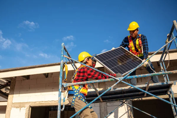 Asian technicians or workers wearing fall protection safety clothing carry solar cells to install on the roof of a house. Concept of alternative and renewable energy.