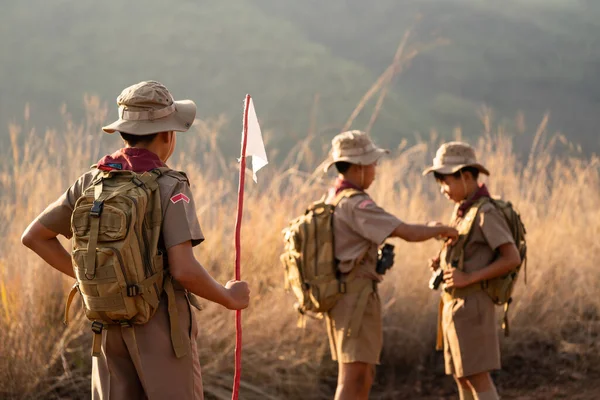 Asian Scout Leader watches as two Scouts in the team inspect each other\'s attire before making the long journey to the Scout camp.