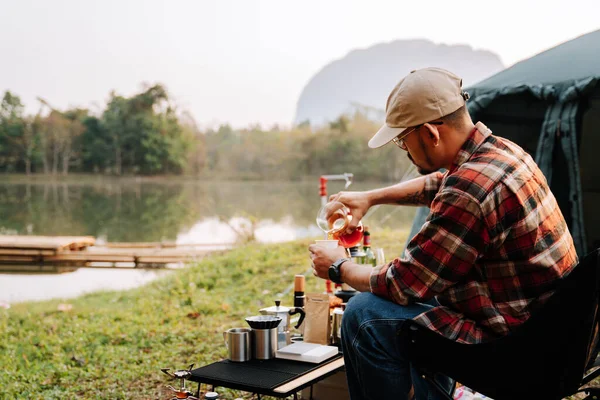 A man drip coffee in the camp near the river in the morning, A man pouring water on coffee ground with filter. Drip coffee and camping. Asian camper.