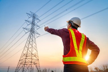Elektrik mühendisi, elektrik enerjisi üreterek ve yüksek voltaj pilonlarına elektrik enerjisi ihraç ederek planlamanın nasıl işlediğini görmek için yüksek voltaj pilonuna bakıyor..