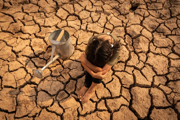 stock image Asian girl and drought. Sad little girl sitting with a watering can on dry ground. Water crisis, Concept hope and drought.