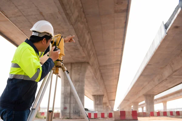 道路工事のセオドライトで高速道路の下で測定を行う男性測量士の技術者 道路建設現場 測量機器の測量エンジニア 高速道路 — ストック写真