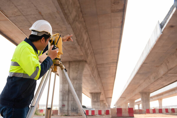 A male surveyor engineers worker making measuring under the expressway with theodolite on road works. Survey engineer at road construction site, Surveyor equipment.  Highway.
