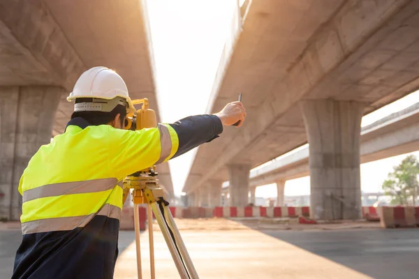 A male surveyor engineers worker making measuring and pointing finger with theodolite on road works. Survey engineer at road construction site, Surveyor equipment. Highway.
