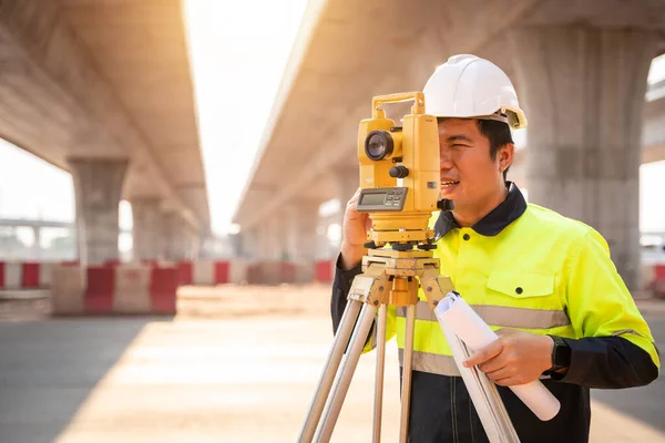 Asian civil engineer or surveyor making measuring under the expressway with theodolite on road works. Survey engineer at road construction site, Surveyor equipment. Highway.