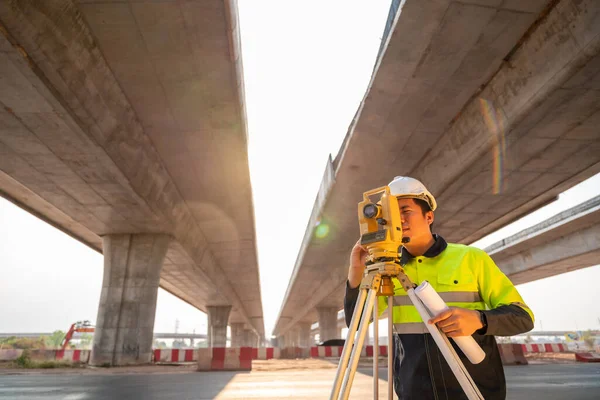 持有蓝图的亚洲土木工程师或测量师 在高速公路下与经纬仪一起进行道路工程测量 公路工地勘测工程师 勘测设备 — 图库照片