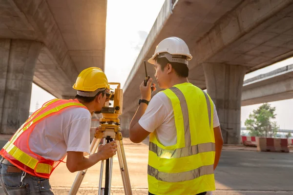 Teamwork of civil engineer and surveyor engineers use radio communication and making measuring with theodolite on road works. Survey engineer at road construction site, Surveyor equipment. Highway.