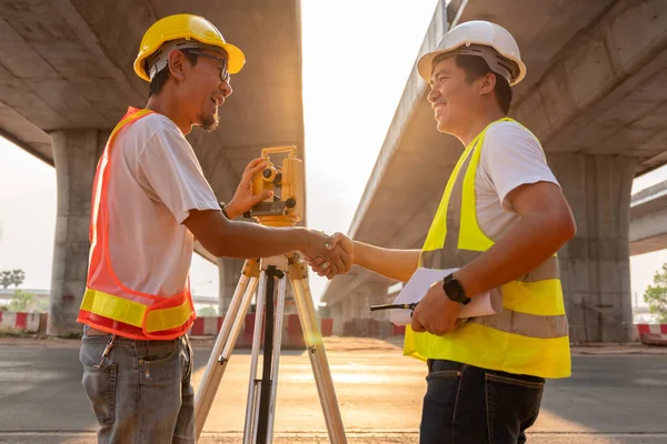 アジアの土木技術者と測量士のエンジニアは 道路建設現場 測量機器で仕事をした後 喜んで握手をします 高速道路 — ストック写真