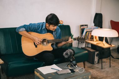 Asyalı bir adam canlı akustik gitar çalıyor ve yaratıcı müzisyenler için taşınabilir müzik kaydedici fikirleri var. Sanatçı, söz yazarı veya besteci, 