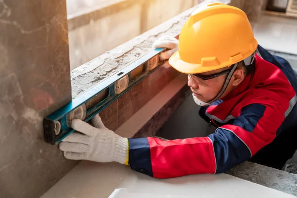 An engineer or inspector wearing safety gear is using the water level to accurately check the construction of a building. Contractor inspection and construction engineering concept.