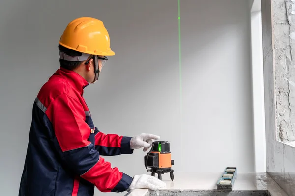 An engineer or construction specialist using laser level instrument to construction and finishing works indoors. Laser construction level with green beams on the wall. Renovation of Construction Work.