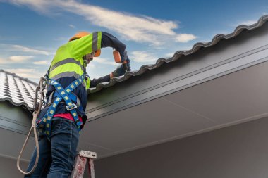 Güvenlik kemeri takan bir Roofer ya da İnşaat işçisi inşaat halindeki evde yeni çatı fayansları kuruyor. Çatı aletleri. Çatı tamiri.