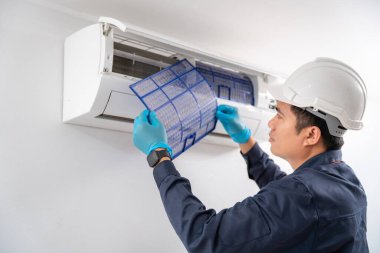 Klima teknisyeni, beyaz duvardaki klimanın tozunu temizlemek için havalandırma filtresini kaldırıyor..