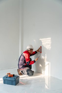 Asyalı mühendis ya da kıdemli uzman inşaat alanındaki bitmemiş bir evde elektrik prizlerini kontrol ediyor. Dikey resim.