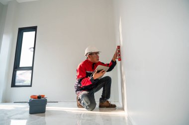 Asyalı mühendis ya da müfettiş alet çantasındaki uzman su seviyesini inşaat alanındaki konut binalarını incelemek için kullanıyor..