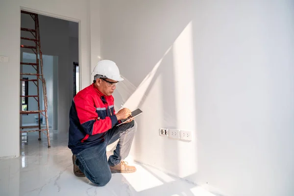 Asian engineer or senior specialist checking electrical outlets in a new unfinished residential house.