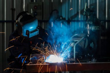 Endüstriyel üniforma giyen bir zanaatkar ya da işçiler çelik kaynak fabrikalarında demir maske takıyor..