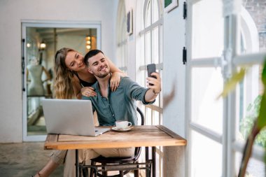 Mutlu çift evde akıllı telefondan selfie çekiyor. İnsanlar ve modern teknoloji kavramı.