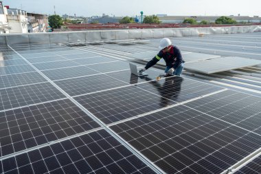 Bir teknisyen endüstriyel fabrikanın çatısındaki güneş panellerinin gücünü kontrol etmek için bir elektrik sayacı ve bir laptop kullanıyor. Güneş enerjisi ya da Temiz Enerji kavramı. 