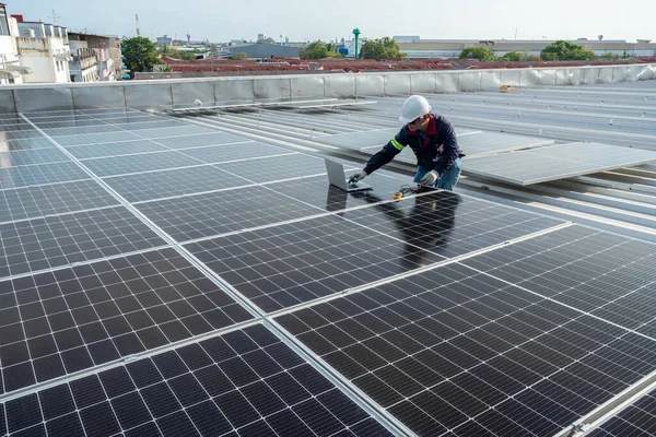 Bir teknisyen endüstriyel fabrikanın çatısındaki güneş panellerinin gücünü kontrol etmek için bir elektrik sayacı ve bir laptop kullanıyor. Güneş enerjisi ya da Temiz Enerji kavramı. 