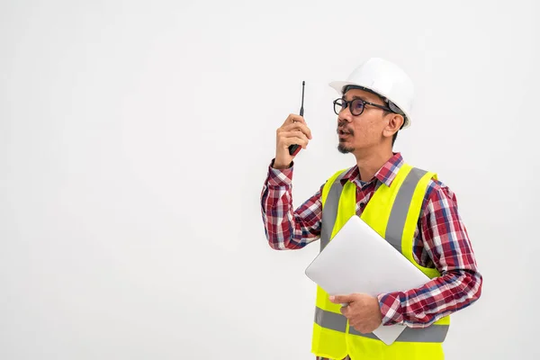 身穿头盔背心的亚洲大胡子建筑工人使用带手提电脑的对讲机站在白色背景上 建筑工头概念 — 图库照片