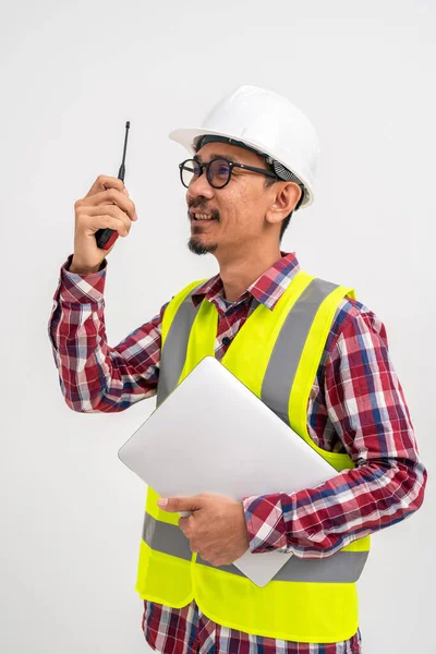 身穿头盔背心的亚洲留胡子土木工程师正在使用带笔记本电脑的对讲机 其背景为白色 建筑工程土木工程概念 垂直图像 — 图库照片