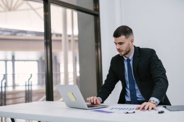 Ofiste çalışırken dizüstü bilgisayar kullanan, masa ve araba anahtarlarını kontrol eden bir araba satıcısı. Galeri ve çevrimiçi satış kavramı.