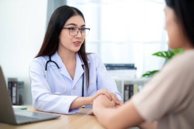 Asyalı kadın doktor, klinikte tedavi ve sağlık hizmetlerini teşvik etmek için kadın hastanın elini tutuyor. Sağlık hizmeti kavramı.