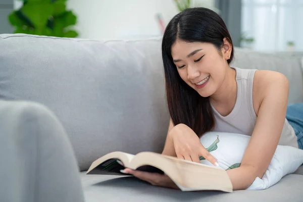 stock image Asian woman lying on the sofa in the living room reading a book happily in the morning.