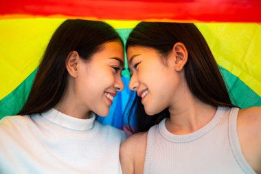 Gökkuşağı bayraklı Asyalı çift destek göstermek için alnı çatışıyor. Lezbiyen gökkuşağı bayrağı. Lezbiyen çift mutlu anların tadını çıkarır..