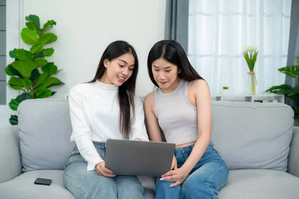 stock image Two young asian women shopping online shopping on laptop while sitting on sofa together in living room.