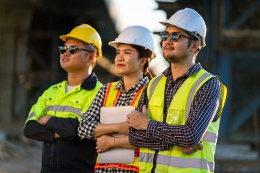 Mimarlar, inşaat mühendisleri, mühendisler ve çeşitlilikten oluşan bir ekip otoban inşaat projesinde kollarını kavuşturarak güvenle duruyorlar..