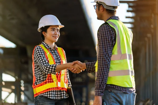 在高速公路建筑工地工作时 戴着防护头盔 身穿反光安全服装的亚洲女建筑师与工程师握手 — 图库照片