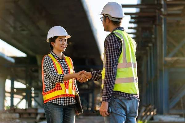アジアの女性建築家や保護ヘルメットやベストの建設労働者は高速道路建設現場で働いている間 エンジニアと握手しています — ストック写真