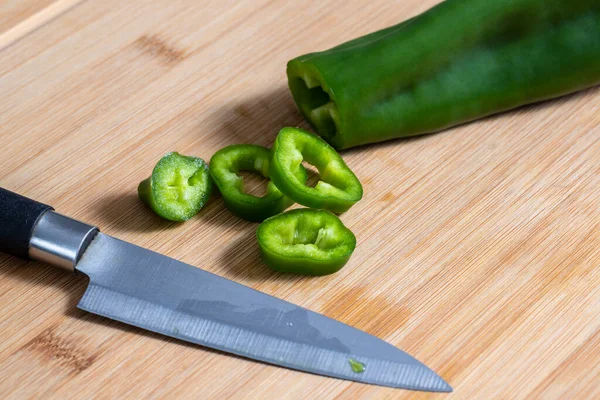 Portions of green bell pepper cut with knife on wooden kitchen board. Food preparation concept. Selective focus