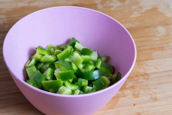 Knife cut green bell pepper portions inside a pink bowl on wooden kitchen board. Food preparation concept. selective focus