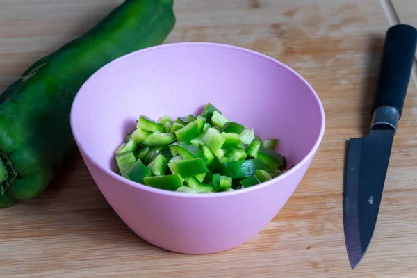 Knife cut green bell pepper portions inside a pink bowl on wooden kitchen board. Food preparation concept. selective focu