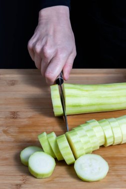 Ahşap mutfak tahtasına kabak kesen odaklı bir kadının elleri. Yemek hazırlama konsepti. Seçici odak