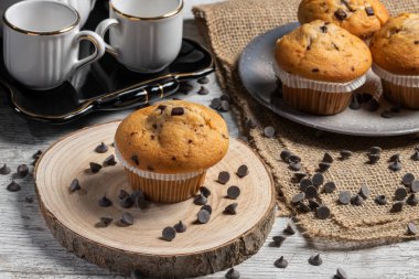 Muffin or cupcake with chocolate chips on wooden table background. Concept of making industrial or homemade pastries. Selective focus.