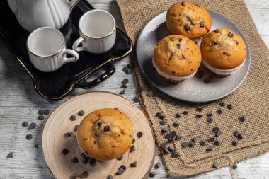 Muffin or cupcake with chocolate chips on wooden table background. Concept of making industrial or homemade pastries. Selective focus.