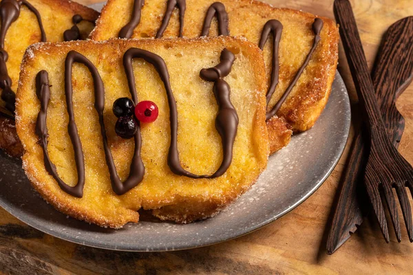 (Torrijas) Fried bread soaked in milk flavored with vanilla, cinnamon, lemon and egg with chocolate on a wooden background.Typical Easter sweet. Concept of traditional festive cuisine.Selective focus.
