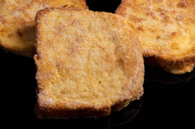 (Torrijas) Fried bread soaked in milk flavored with vanilla, cinnamon, lemon and egg on a black background. Typical Easter sweet. Concept of traditional and festive cuisine. Selective focus.