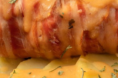 Sosuna domuz pastırması sarılmış peynirle doldurulmuş tavuk göğsü, kilden bir tencerede fırınlanmış patatesler. Zengin ve lezzetli mutfak kavramı. Yatay fotoğraf ve seçici odak.