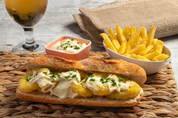 Tipik İspanyol kalamar sandviçi. Mayonez, sarımsak ve maydanozlu. Biraz kızarmış patates ve bir bardak soğuk bira. Tapas kavramı, eğlence ve gastronomi. Yatay fotoğraf ve seçici odaklanma..