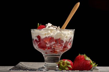 Süslü tabakta kremalı ve çikolatalı çilekli tatlı bardağı siyah arka planda. Yatay fotoğraf ve seçici odak