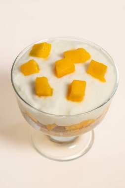 Beyaz zemin üzerinde mango ve bisküvi bulunan lezzetli bir bardak soğuk yoğurt kreması. Tarif veya menü için dikey fotoğraf ve seçici odak